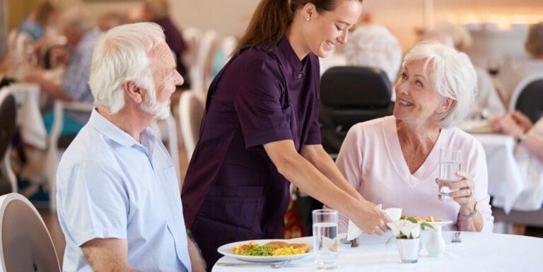 Senior Couple Served Meals by Female Nursing Staff in Independent Living Facility
