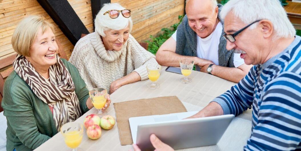 Elderly Group Smiling While Using Laptop Outdoors At Independent Living Facility